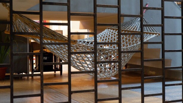 A hammock suspended between metal bars in a room with a staircase and a potted plant. - Leisure Hostel (Krabi)