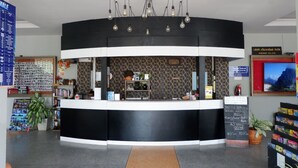 A reception area with a black and white counter, a patterned wall, and a chandelier. There are signs for shuttle services and a local dining area. - Leisure Hostel (Krabi)