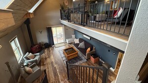 Ein geräumiges Loft mit hoher Decke, Holzbalken, einem Balkon und einer gemütlichen Sitzecke mit Kamin.