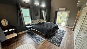 Ein Schlafzimmer mit einem großen Bett, einem Schminktisch mit Spiegel, einem kleinen runden Tisch und einem Fenster mit Vorhängen.
