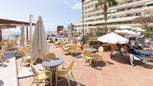 Een terras op het dak met buitenmeubilair, palmbomen en uitzicht op een hotelgebouw.