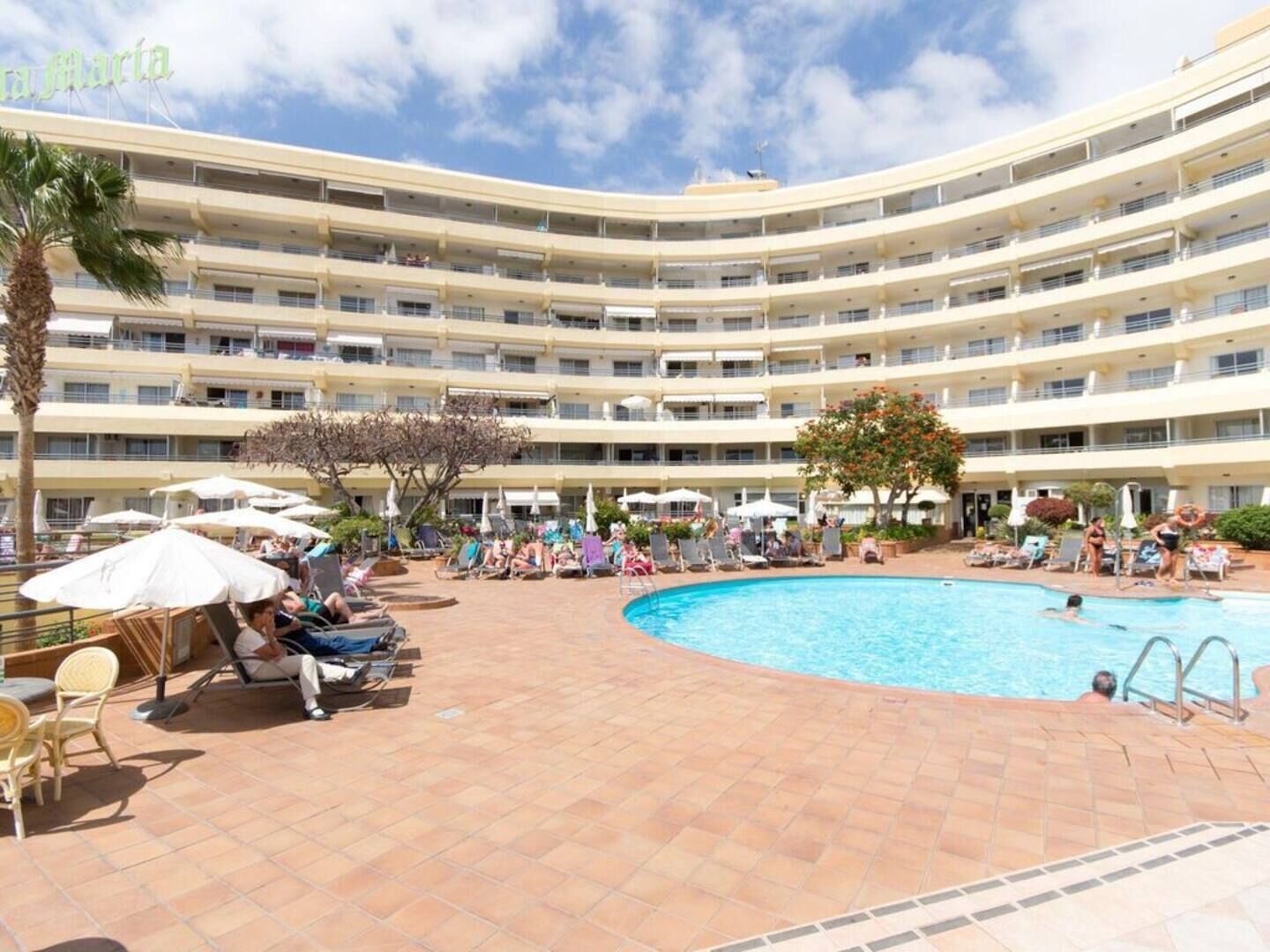 A multi-story hotel with a central swimming pool surrounded by sun loungers and umbrellas.