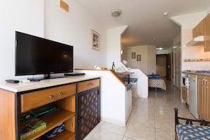 A modern kitchen with a flat-screen TV, wooden cabinets, and a dining area with a table and chairs.