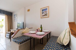 A dining area with a table set for two, a television, and a window with curtains.