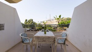 Un balcon avec une table et des chaises, une bouteille, et une vue sur une colline parsemée de bâtiments.