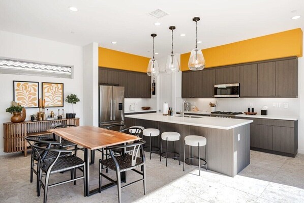 A modern kitchen with a central island, bar stools, and pendant lighting. - PGA West: Your Poolside & Fire Pit Haven (La Quinta)