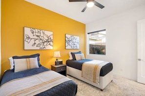 A bedroom with two beds, a ceiling fan, and artwork on the walls. - PGA West: Your Poolside & Fire Pit Haven (La Quinta)