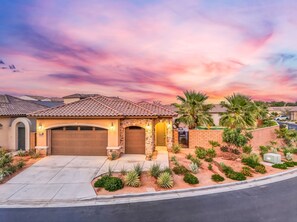 A residential house with a garage, a stone entrance, and a landscaped garden with various plants. - PGA West: Your Poolside & Fire Pit Haven (La Quinta)