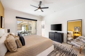 A modern bedroom with a large bed, a flat-screen TV, a ceiling fan, and a sliding glass door leading to a dining area.