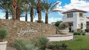 Signature at PGA West features a grand stone entrance with a beautifully landscaped lawn and palm trees.