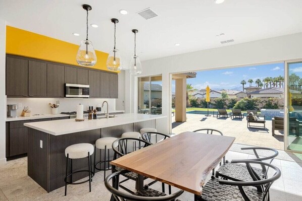 A modern kitchen with a central island, bar stools, and a dining table with chairs.