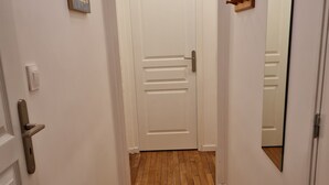 Un pasillo con piso de madera, paredes blancas y una puerta blanca con manija.