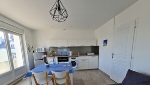 Cocina compacta con armarios blancos, lavadora y zona de comedor con mantel azul.