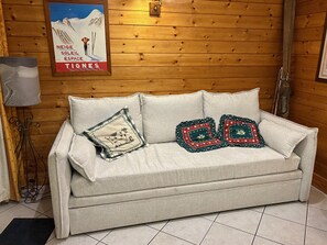 Un sofá blanco con dos almohadones decorativos frente a una pared de madera.