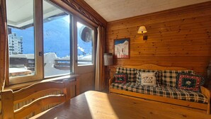 Ein gemütliches Blockhaus-Interieur mit einer hölzernen Bank, einem Karomuster-Sofa und einem großen Fenster mit Blick auf eine verschneite Landschaft.