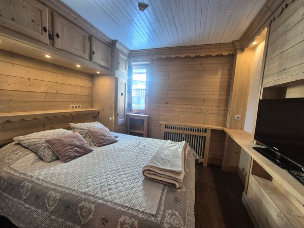 Una habitación de cabaña de madera con una cama, un televisor y una ventana.