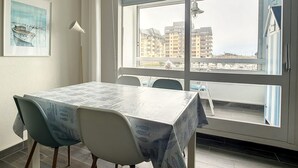 Een eethoek met een tafel en stoelen, een raam met uitzicht op gebouwen, en een schilderij aan de muur.