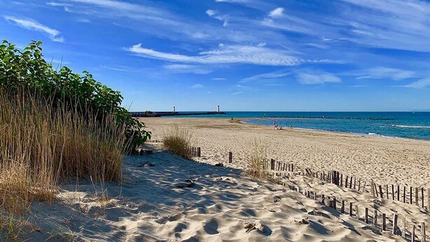 Une plage avec une clôture en bois, un rivage sablonneux et un phare à l’horizon.
