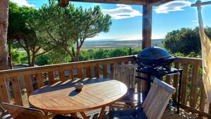 Une terrasse en bois avec une table ronde et des chaises, un barbecue et une vue sur le paysage.