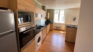 Une cuisine moderne avec des meubles en bois, des appareils électroménagers en acier inoxydable, un lave-linge intégré et une grande fenêtre qui laisse entrer la lumière naturelle.