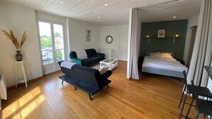Une pièce spacieuse avec un canapé vert, un lit, un plancher en bois et une grande fenêtre donnant sur l’extérieur.