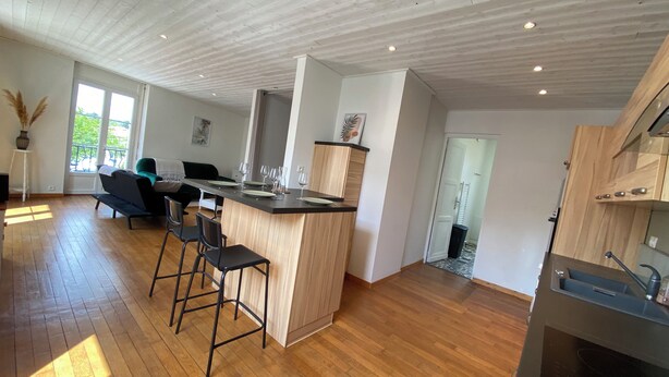 Une cuisine moderne avec un îlot central en bois, des tabourets de bar et un coin repas comprenant un canapé et des chaises.