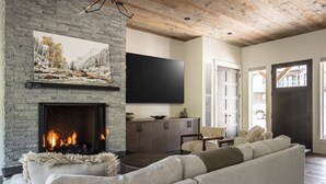 Una sala de estar con chimenea de piedra, televisor de pantalla plana, sofá y vista al exterior.