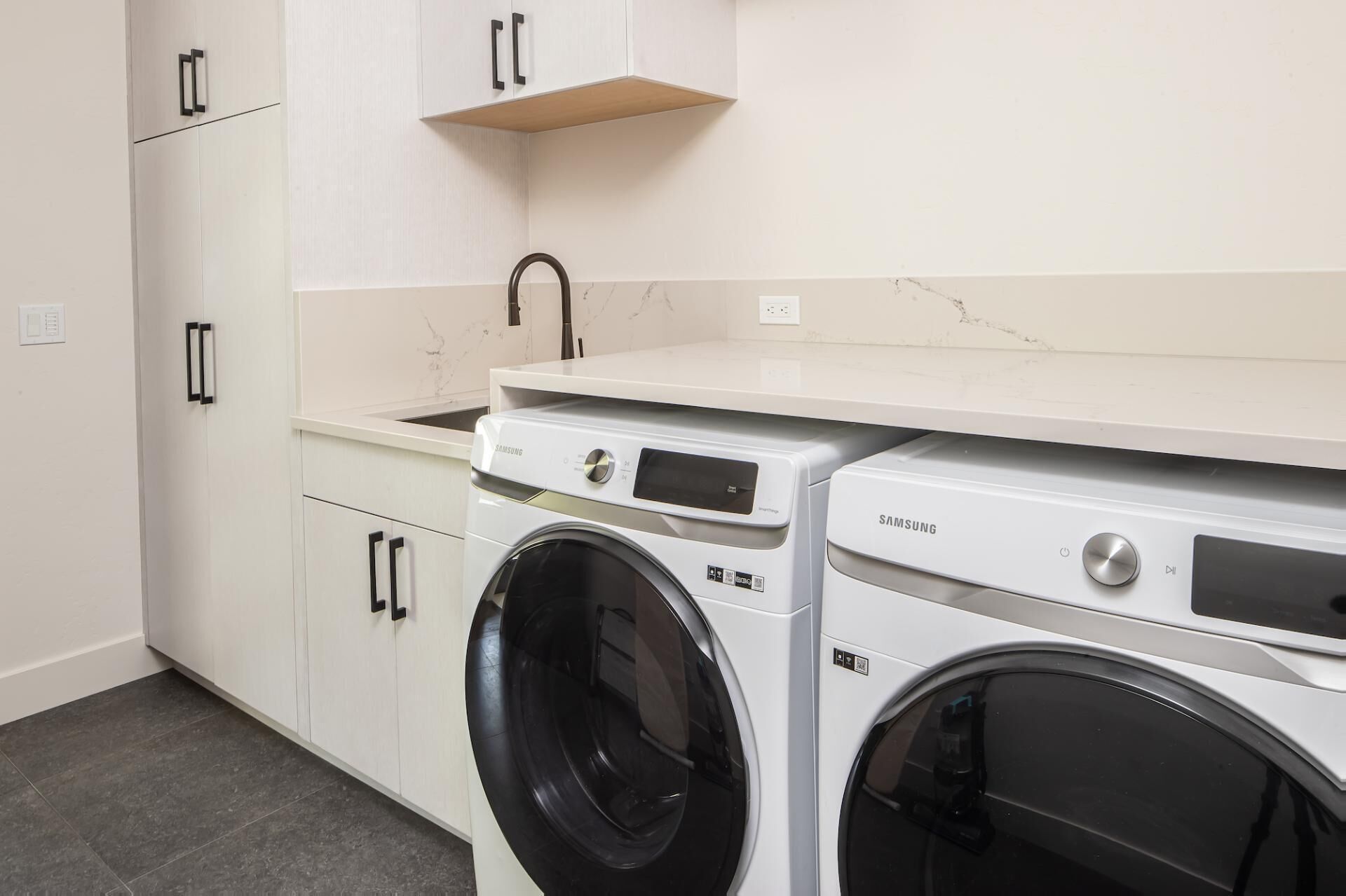Un espace buanderie équipé d’un lave-linge et d’un sèche-linge, de meubles blancs et d’un pare-feu en marbre.