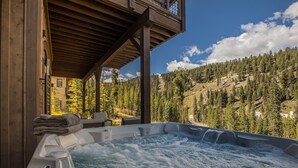 Un jacuzzi con cubierta de madera y vista a una cadena montañosa boscosa.
