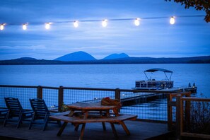 Ein Steg am See mit Tisch und Stühlen, ein Boot liegt an einem Steg festgemacht, und Berge im Hintergrund.