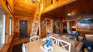 A wooden cabin interior with a dining area, a staircase, a living room with a sofa and a TV, and a kitchen area. - Sleeps 25! Book all 5 Lawrence`s Lakeside Cabins! (Rockwood)
