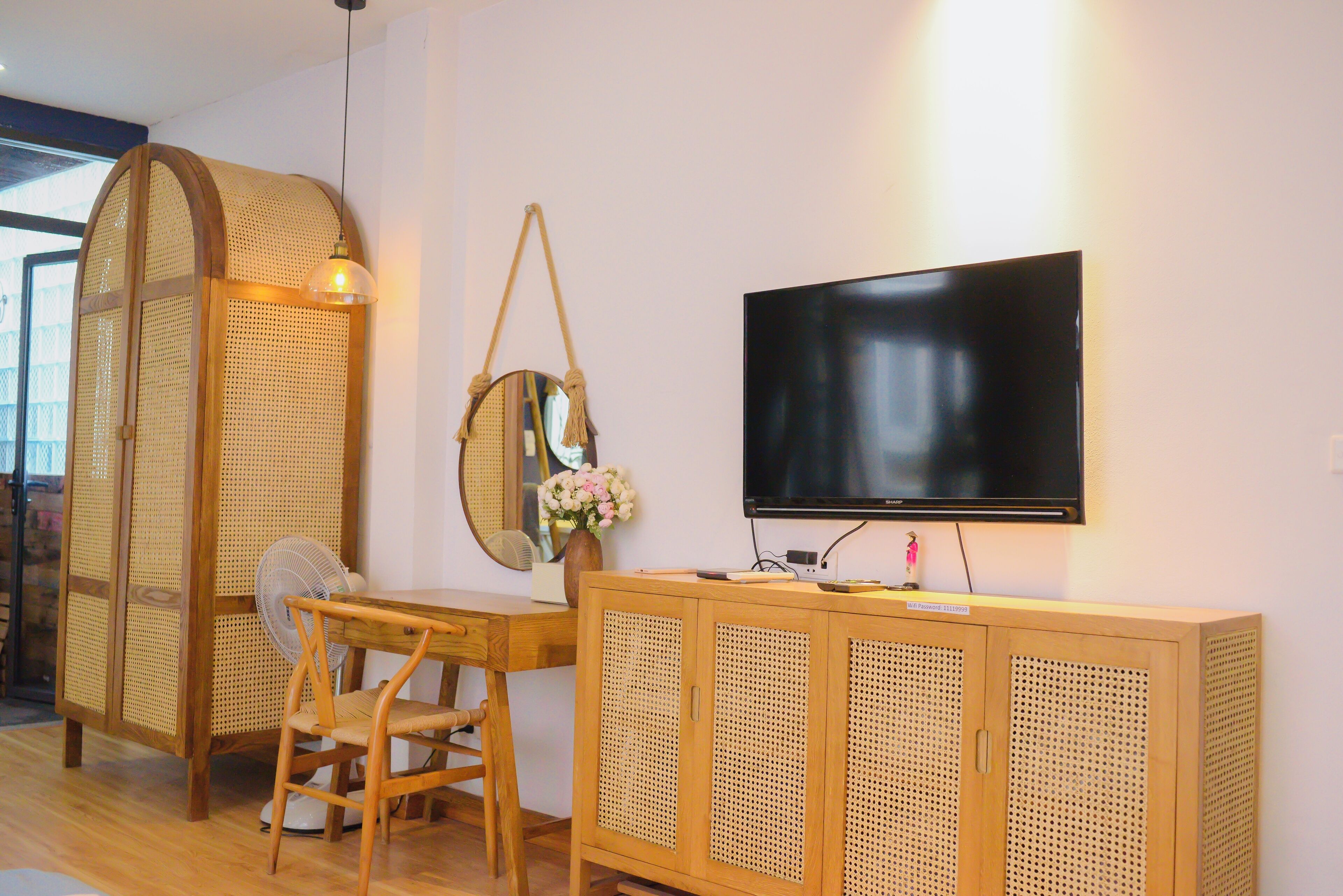 A room with a wooden desk, a chair, a television mounted on the wall, and a woven partition.