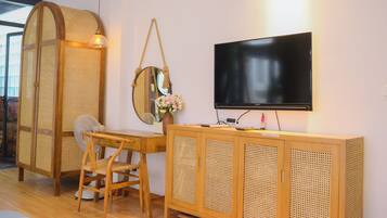 A room with a wooden desk, a chair, a television mounted on the wall, and a woven partition.