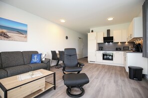Una sala de estar moderna con un sofá, una mesa de comedor y una zona de cocina con armarios y electrodomésticos blancos.