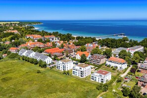Vue aérienne d’une zone résidentielle côtière, avec des maisons, une jetée et une vue dégagée sur la mer.