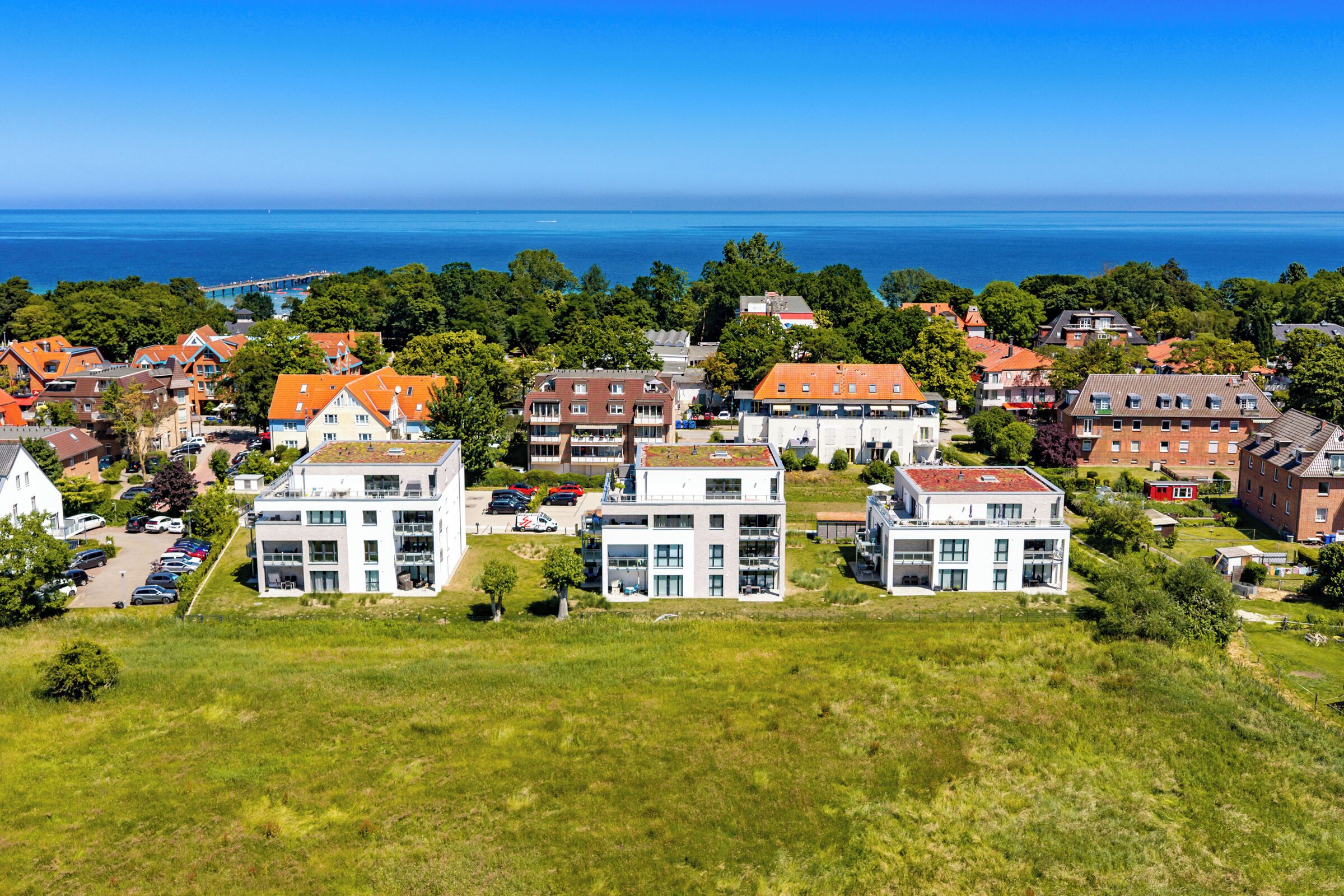 A coastal residential area with modern and traditional buildings, a clear view of the sea, and a bridge in the distance.