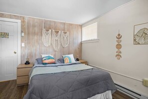 Une chambre à coucher avec un lit, un mur recouvert de panneaux en bois, des décorations murales en macramé et des œuvres d’art accrochées au mur.