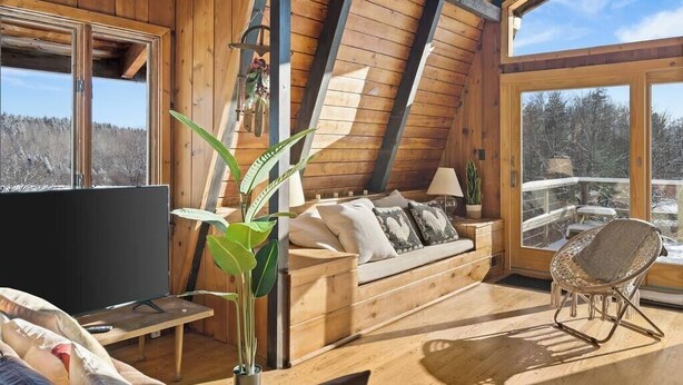A cozy wooden cabin interior with a sofa, a TV, and a chair. - Cozy Mt. Snow Cabin w/ Fireplace (Wilmington)