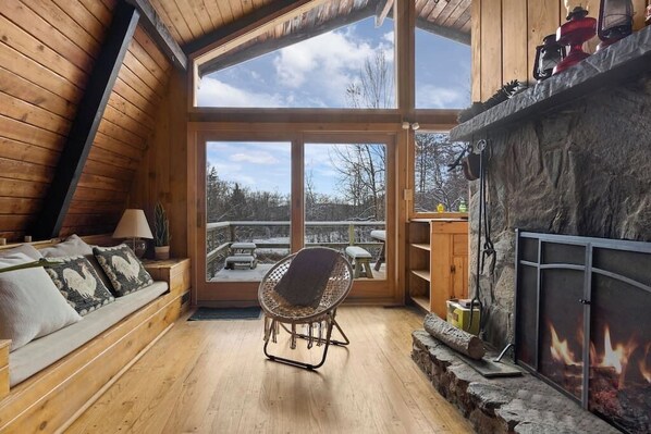 Un intérieur chaleureux en bois, avec une cheminée en pierre, un coin salon confortable et une vue sur le paysage enneigé.