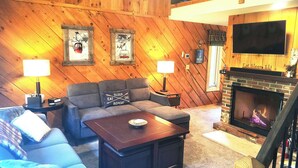 A cozy living room with a fireplace, wooden walls, a sofa, a coffee table, and two lamps.
