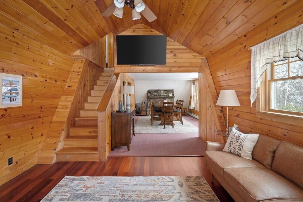 L’intérieur d’un chalet en bois comprend un escalier menant à une salle à manger, un canapé et un téléviseur à écran plat fixé au mur.