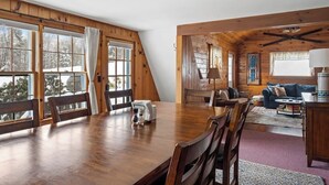A cozy cabin-style room with a wooden dining table, chairs, and a sofa.