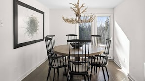 A dining room with a round table and six chairs, a chandelier, and a framed artwork on the wall. - Updated Condo Close to Mt Snow! (Wilmington)