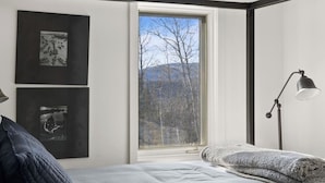 A bedroom with a large window, a bed, a bedside lamp, and two framed pictures on the wall. - Updated Condo Close to Mt Snow! (Wilmington)