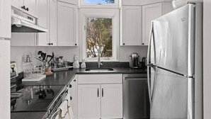 A modern kitchen with white cabinets, a stainless steel refrigerator, and a window above the sink. - Updated Condo Close to Mt Snow! (Wilmington)