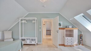 A bedroom with a sloped ceiling, a bed, a wardrobe, a chest of drawers, and a bookshelf. - Domizil am Eschenweg 5 Appartement Ostseerauschen (Scharbeutz)