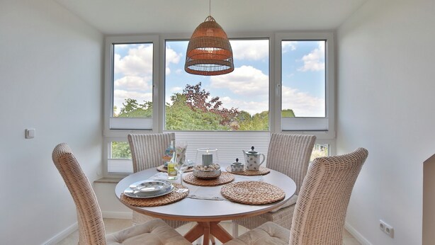 A dining area with a round table, wicker chairs, and a hanging light fixture. - Domizil am Eschenweg 5 Appartement Ostseerauschen (Scharbeutz)