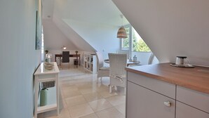 A modern kitchen with a wooden countertop, white cabinetry, and a dining area with wicker chairs. - Domizil am Eschenweg 5 Appartement Ostseerauschen (Scharbeutz)