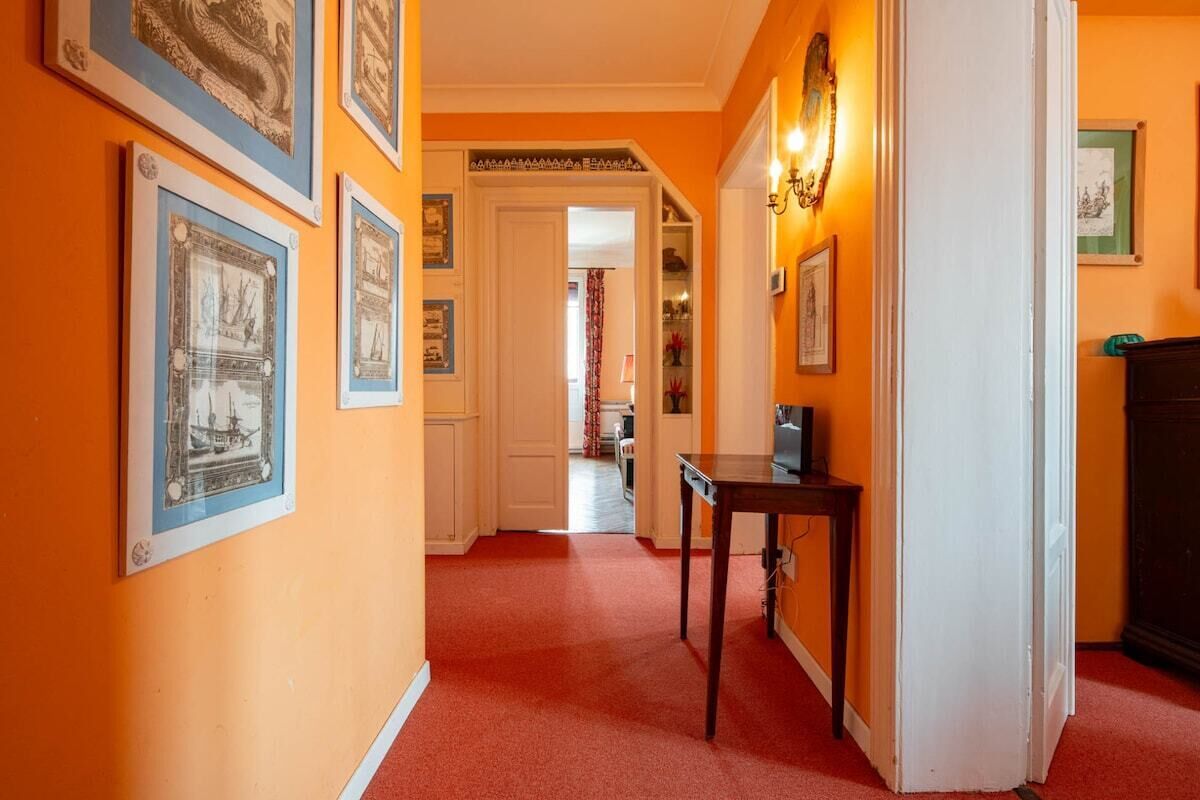 Een hal met kunstwerken in lijsten aan de muren, een tafel en een deur naar een andere kamer.