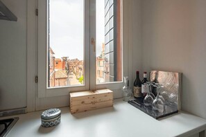 A window with a view of a cityscape, a wooden box, a bottle, and a glass set on a white counter. - Casa Golena (Venezia)